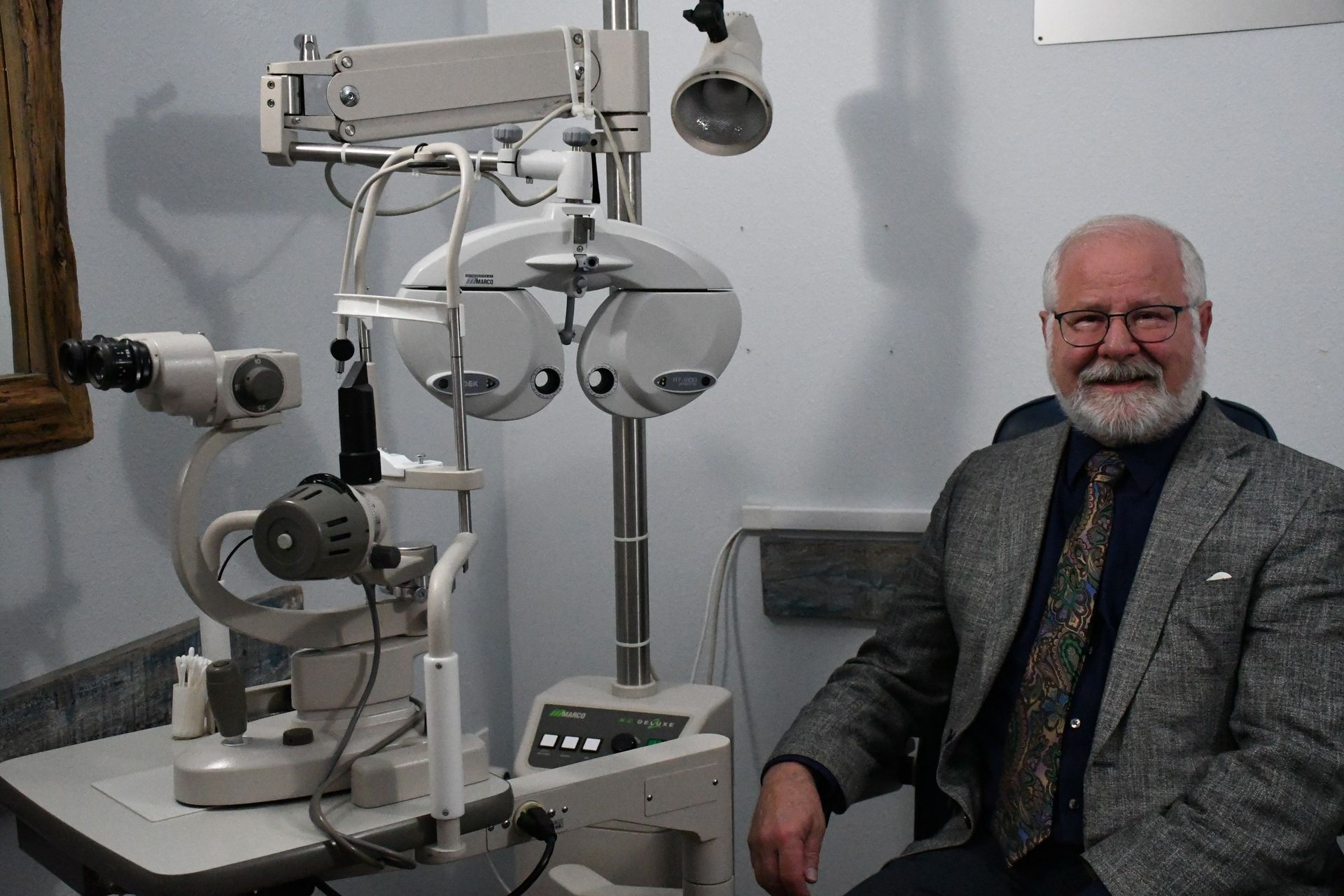 Dr. John Prewett seated beside the slit lamp and phoropter in an exam room