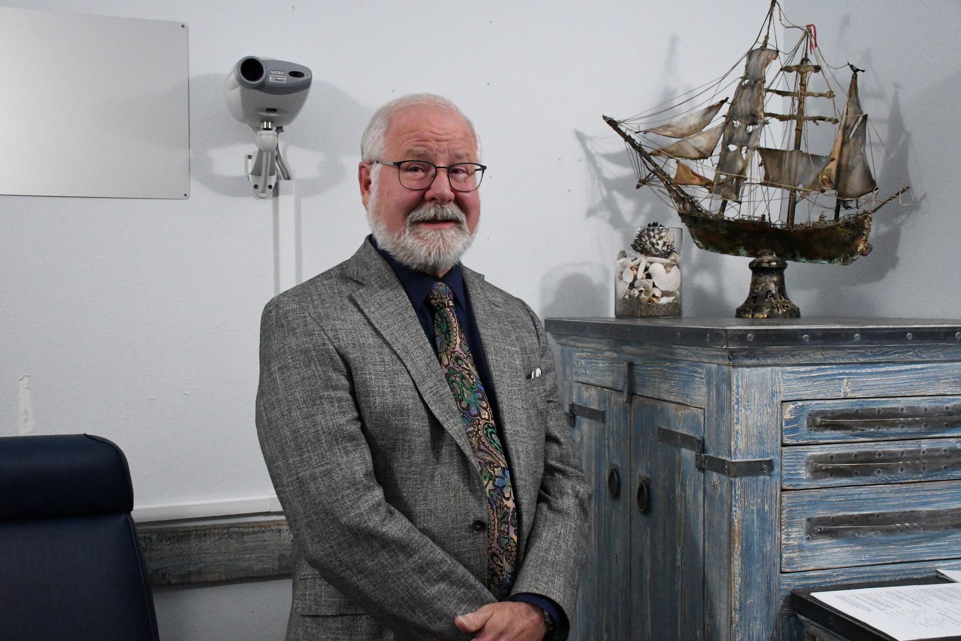 Dr. John Prewett standing beside a blue cabinet topped with a model sailing ship